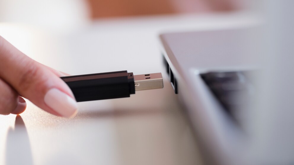Frau hält USB-Stick vor Laptop