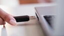 Frau hält USB-Stick vor Laptop