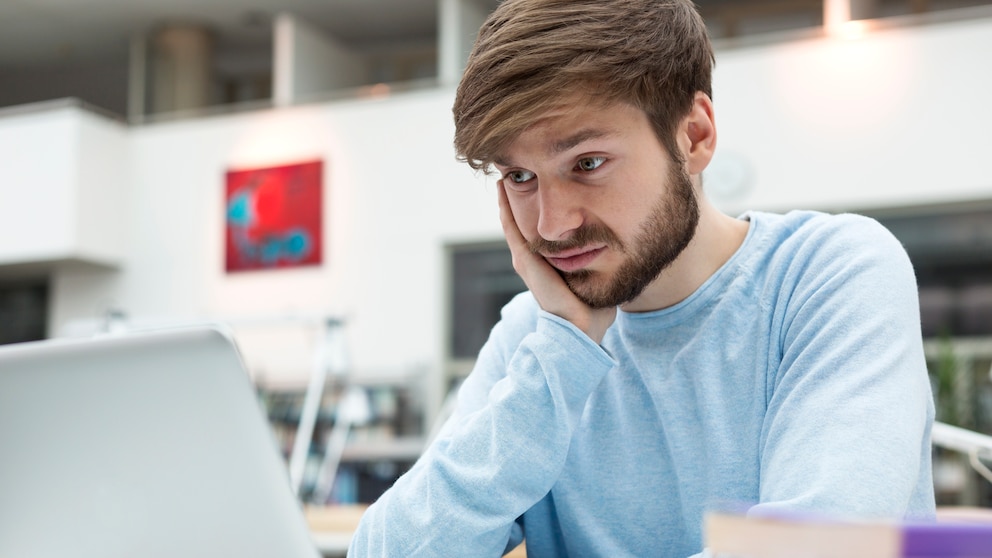 junger Mann schaut unglücklich auf seinen Laptop