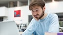 junger Mann schaut unglücklich auf seinen Laptop