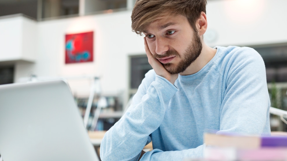 junger Mann schaut unglücklich auf seinen Laptop