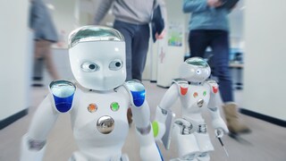 Zwei Roboter laufen im Büro neben Menschen