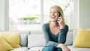 Blonde Frau sitzt auf dem Sofa und telefoniert mit dem Smartphone.