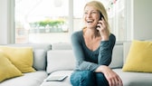 Blonde Frau sitzt auf dem Sofa und telefoniert mit dem Smartphone.