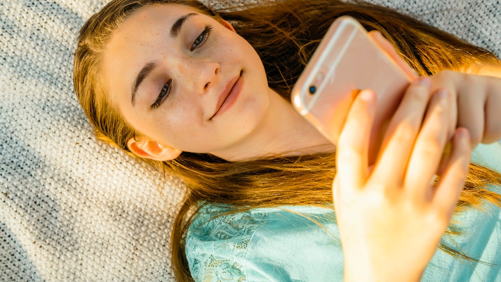 Mädchen liegt auf Decke und schaut auf ihr iPhone.