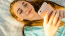 Mädchen liegt auf Decke und schaut auf ihr iPhone.