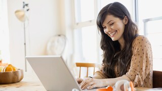Lächelnde Frau sitzt am Tisch und schaut auf Laptop