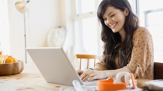 Lächelnde Frau sitzt am Tisch und schaut auf Laptop