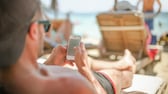 Ein Mann mit Basecap liegt auf Strandliege und schaut auf sein Smartphone