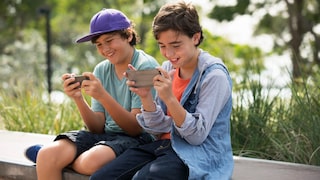 Zwei Jungen sitzen nebeneinander und spielen Spiele-Apps auf ihren Handys