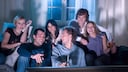 Eine Gruppe von Freunden schaut lachend auf einen Fernseher_Comedy-Serien