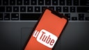 Das Logo von Youtube auf dem Display eines Smartphones vor einer Laptop-Tastatur