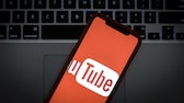 Das Logo von Youtube auf dem Display eines Smartphones vor einer Laptop-Tastatur