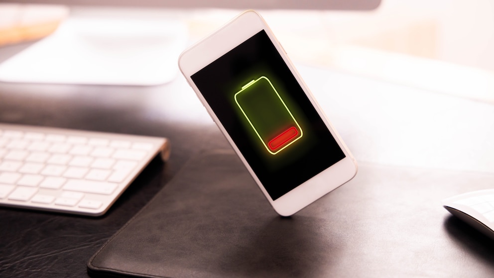 Ein Handy schwebt mit einem sehr geringen Akkustand auf dem Display über einem Schreibtisch