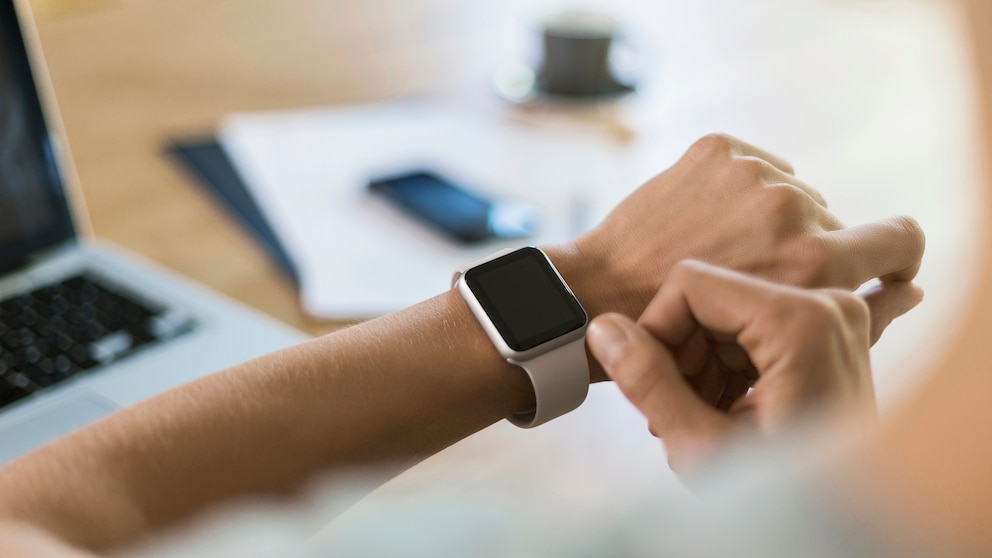Frau am Schreibtisch schaut auf Smartwatch