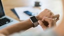 Frau am Schreibtisch schaut auf Smartwatch
