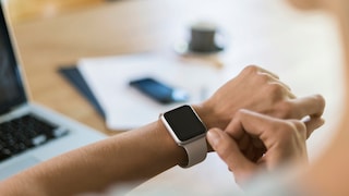 Frau am Schreibtisch schaut auf Smartwatch