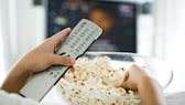 Sky Januar 2020: Person hält Fernbedienung und Popcorn, im Hintergrund ein Fernseher