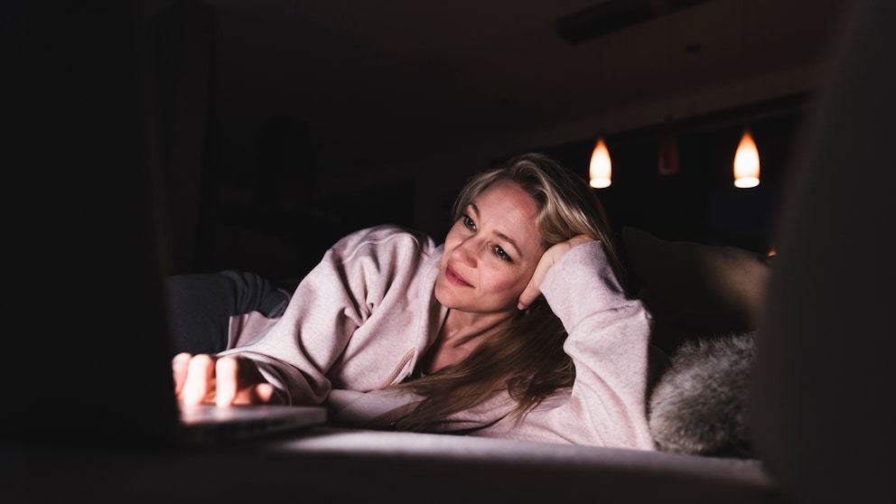 Eine Frau liegt im Bett und schaut auf ihren Laptop