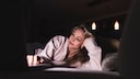 Eine Frau liegt im Bett und schaut auf ihren Laptop