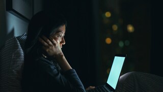 Nachdenkliche Frau sitzt mit MacBook im Bett