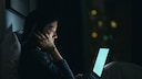 Nachdenkliche Frau sitzt mit MacBook im Bett