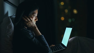 Nachdenkliche Frau sitzt mit MacBook im Bett