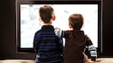 Netflix kindersicher machen mit der Kindersicherung Symbolbild: Zwei kleine Jungen sitzen vor dem Fernseher mit dem Rücken zur Kamerai