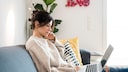 Symbolbild Streaming: Frau sitzt mit ihrem Laptop auf dem Sofa