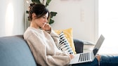Symbolbild Streaming: Frau sitzt mit ihrem Laptop auf dem Sofa