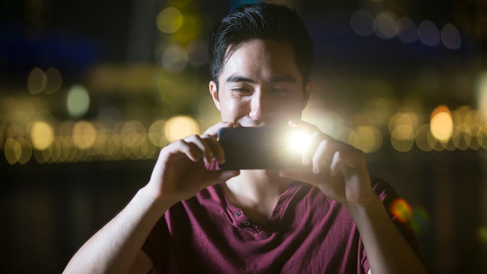 Blitz oder Nachtmodus Symbolbild: Mann macht mit seinem Handy ein Foto und verwendet dabei Blitz