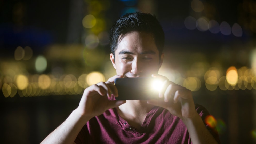 Blitz oder Nachtmodus Symbolbild: Mann macht mit seinem Handy ein Foto und verwendet dabei Blitz