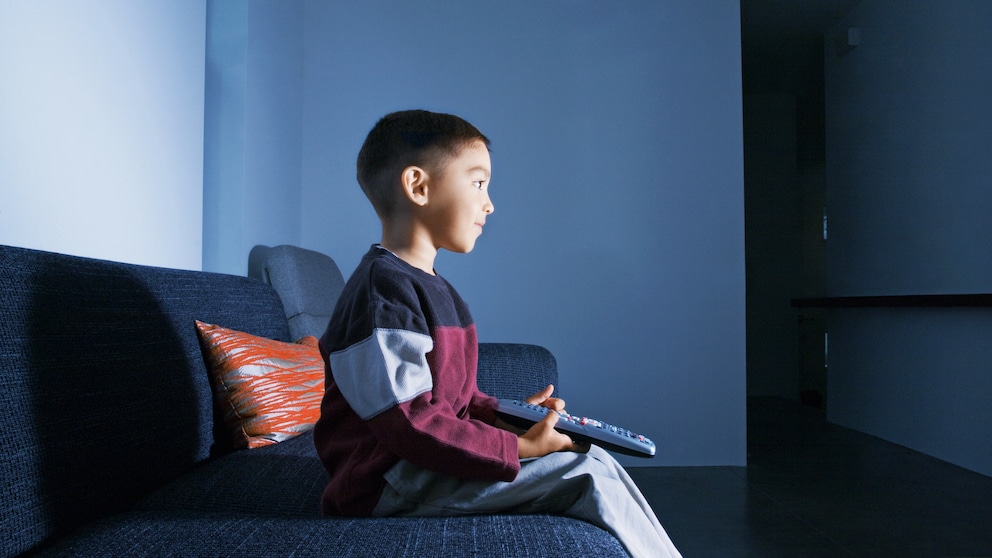 Netflix und Amazon Prime Video für Kinder Symbolbild: Ein kleiner Junge sitzt mit der Fernbedienung in der Hand auf dem Sofa