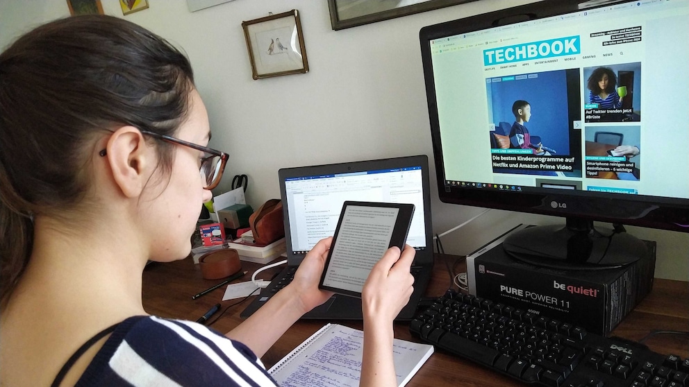 Amazon Kindle Oasis Test: Frau sitzt am Tisch und hält E-Book-Reader in der Hand