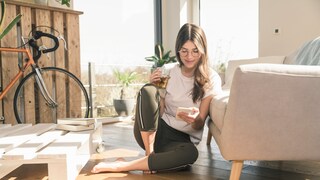 Google Play Store Symbolbild: Frau sitzt mit ihrem Handy vor dem Sofa
