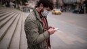 Mann mit Maske und Smartphone auf leerer Straße