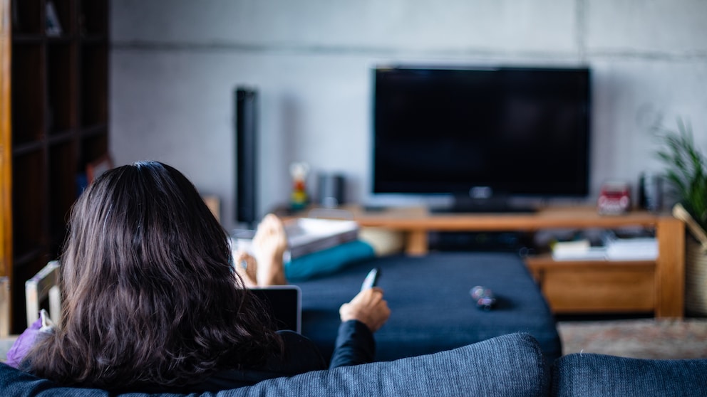Frau sitzt im Wohnzimmer vor dem Fernseher