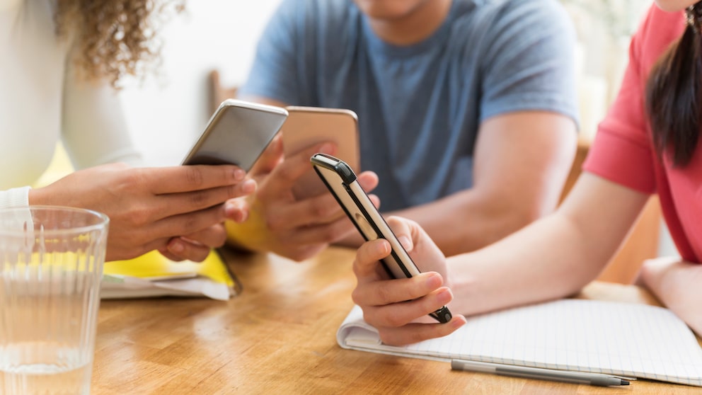 Drei junge Menschen mit Smartphone am Tisch