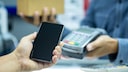 Hand hält Smartphone an Lesegerät zur kontaktlosen Bezahlung