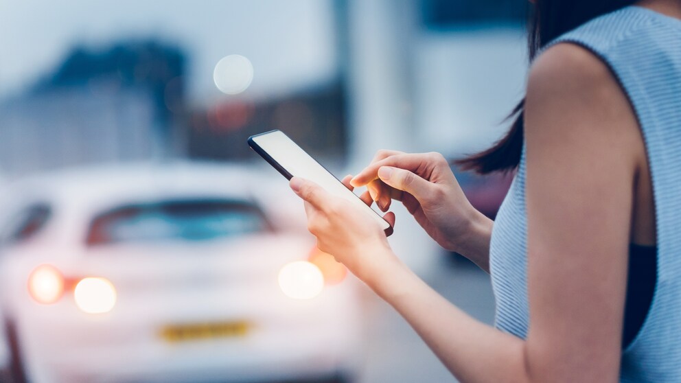 Frau mit Smartphone vor Auto