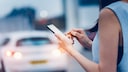 Frau mit Smartphone vor Auto