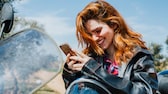 Frau mit Smartphone auf dem Motorrad