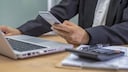 Finanz-Apps: Mann am Computer mit Smartphone und Taschenrechner