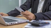 Finanz-Apps: Mann am Computer mit Smartphone und Taschenrechner