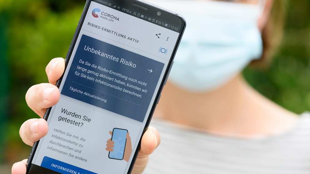 Frau mit Maske hält Smartphone mit Corona-App hoch