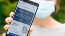Frau mit Maske hält Smartphone mit Corona-App hoch