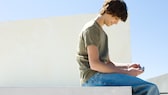 Microsoft xCloud Mobile Gaming: Junge mit Smartphone sitzt draußen