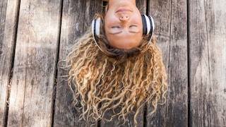 Musik-Streaming-Dienst: junge Frau liegt auf dem Boden und hört mit Kopfhörern Musik