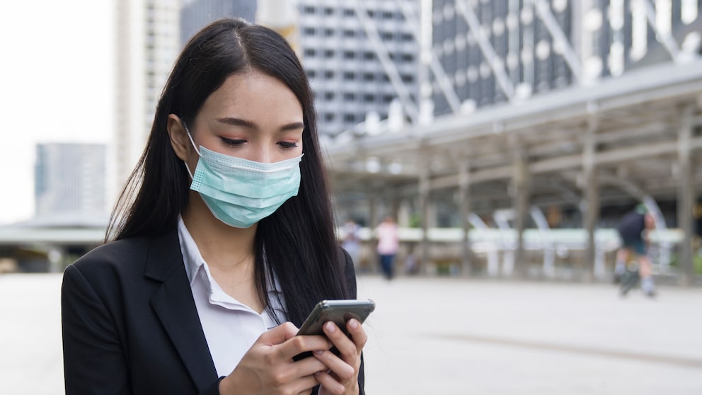 Corona App Update: junge Frau mit Maske schaut auf Smartphone