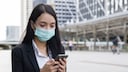 Corona App Update: junge Frau mit Maske schaut auf Smartphone
